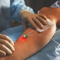 Medical professional inserting an intravenous (IV) catheter into a patient's arm, with a red light indicating the insertion point.