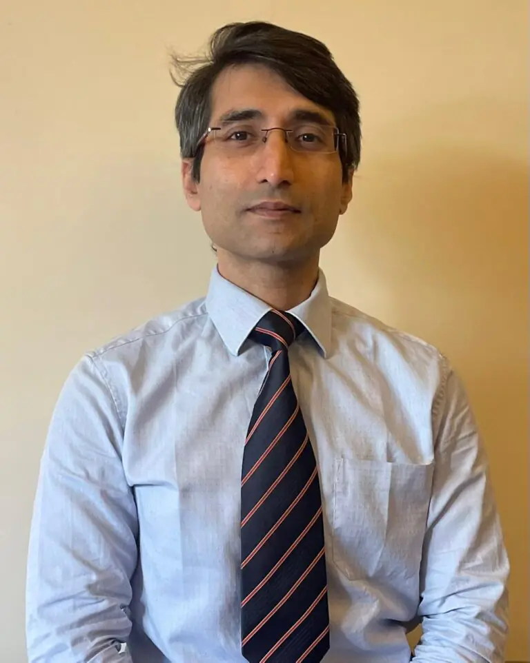 Portrait of Dr. S. Narayan, a South Asian man wearing glasses, a light blue shirt, and a striped tie, standing against a neutral background.